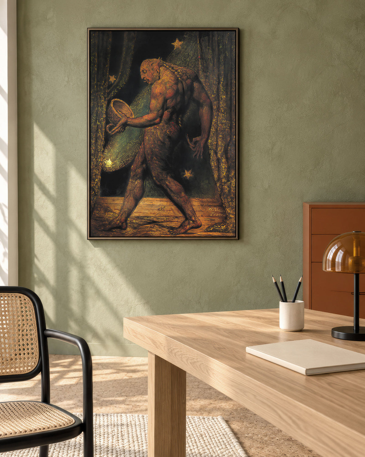 A framed art print depicting a muscular nude figure holding a tennis racket in a dark forest with stars, displayed on a textured sage green wall above a wooden desk in a modern home office setting.