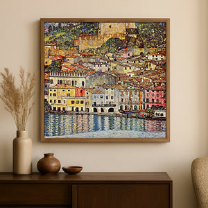 A framed square canvas print of an impressionist coastal town painting hangs on a beige wall above a dark wood console table with decorative vases.